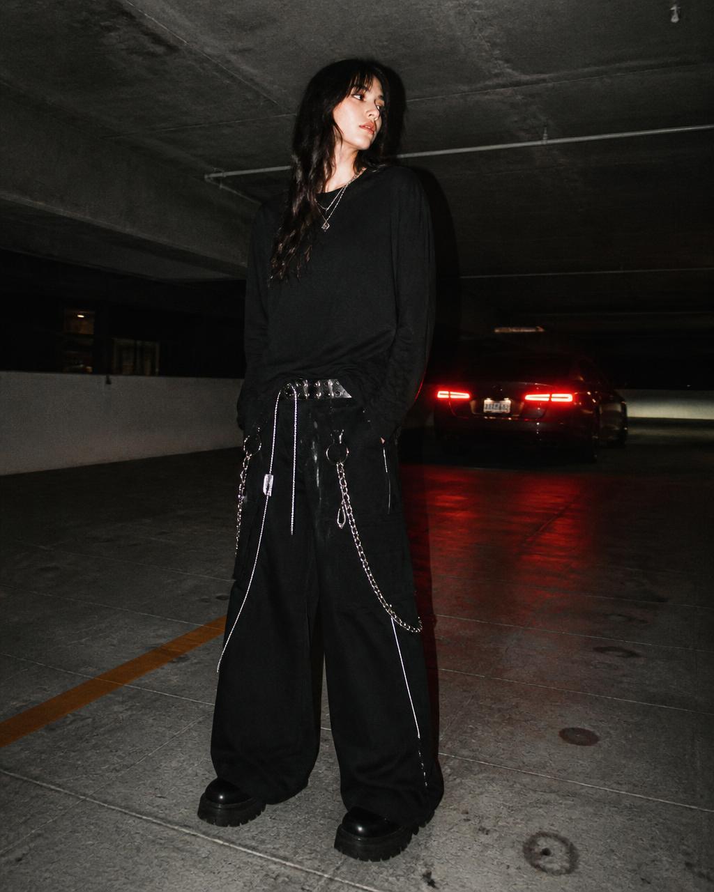 Model in black long sleeve and wide chained trousers in a dim parking garage