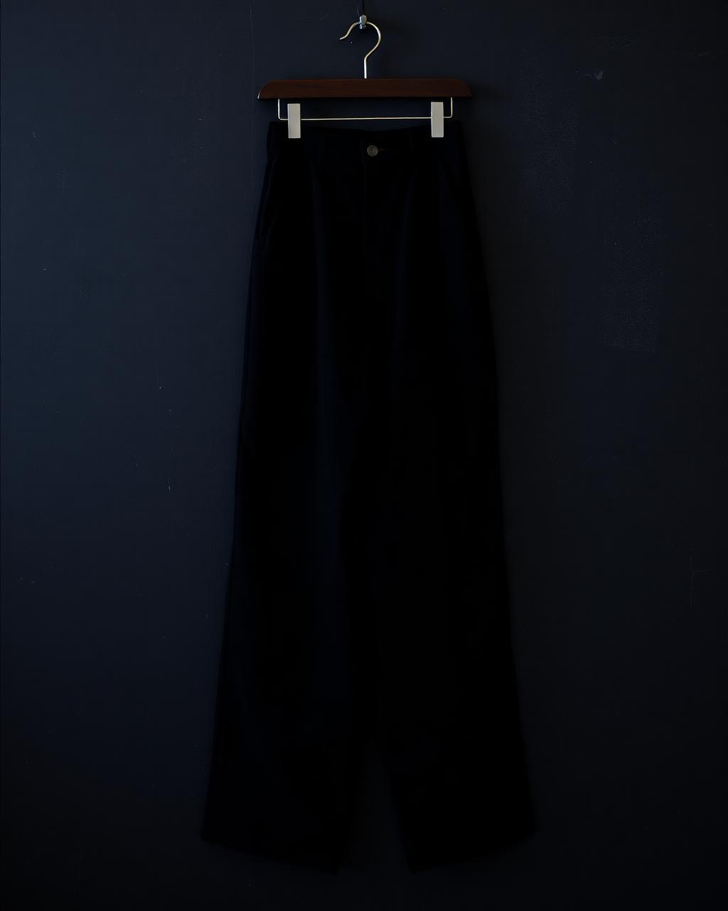 Wide-leg black washed canvas trousers hanging against a dark wall